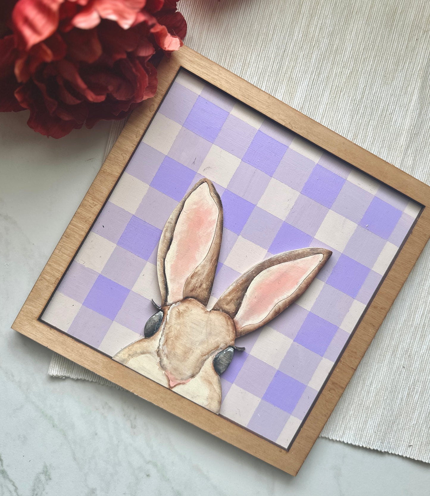 A peekaboo hand painted mouse brown bunny sign over a purple plaid backer with a stained frame.