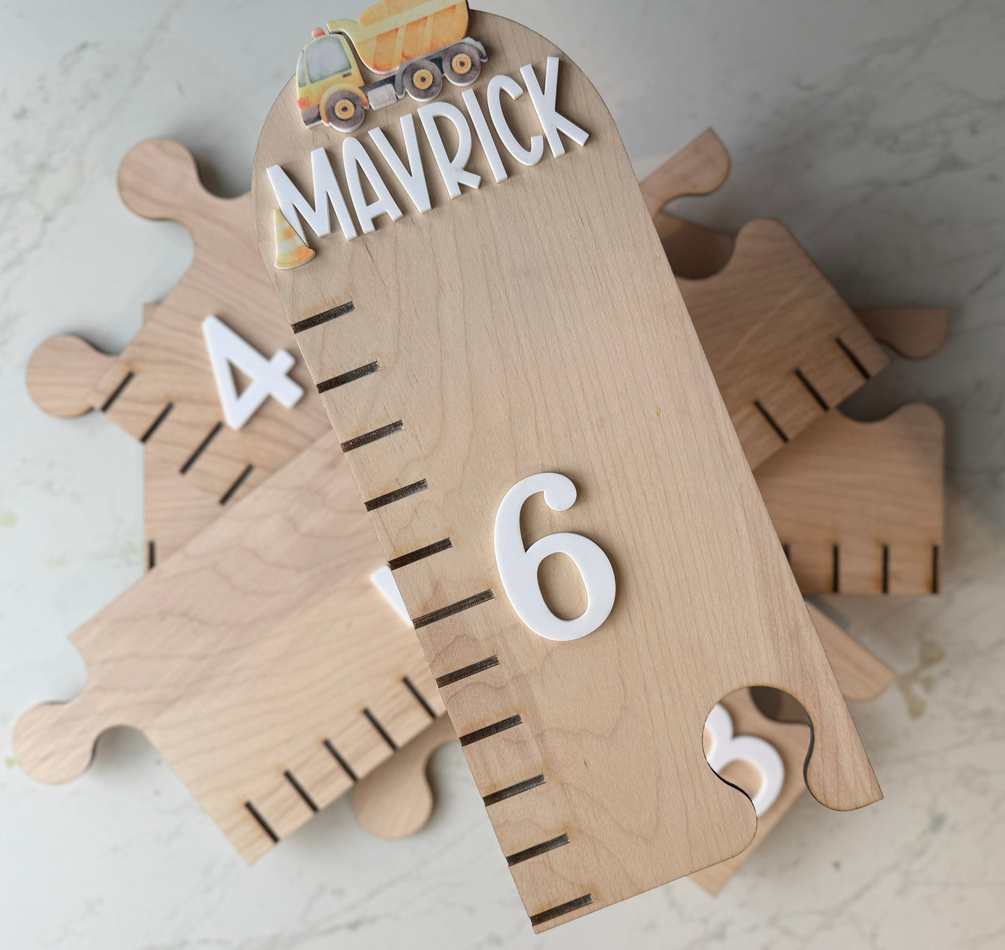 Wooden growth chart with puzzle pieces and numbers on a light background featuring a dump truck and the name ‘mavrick’