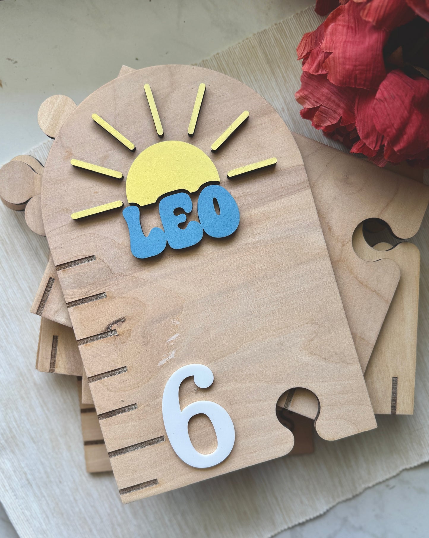 Wooden puzzle piece with 'LEO' and number '6', sun design, on a light background.