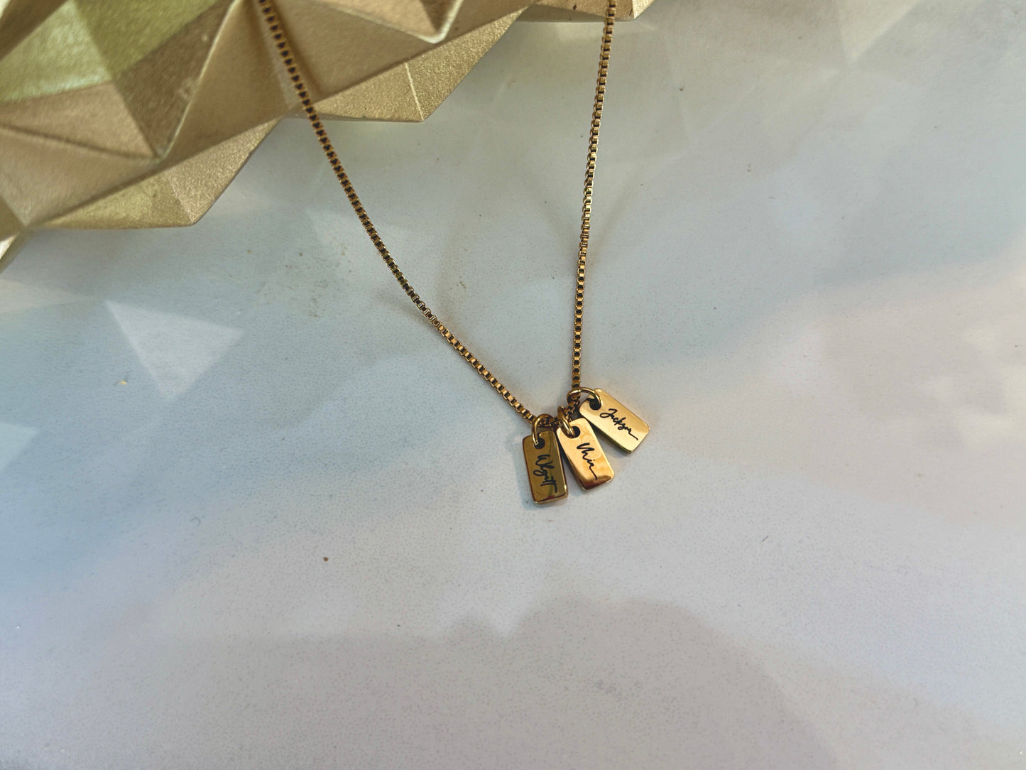 Gold necklace with two tags on a light background