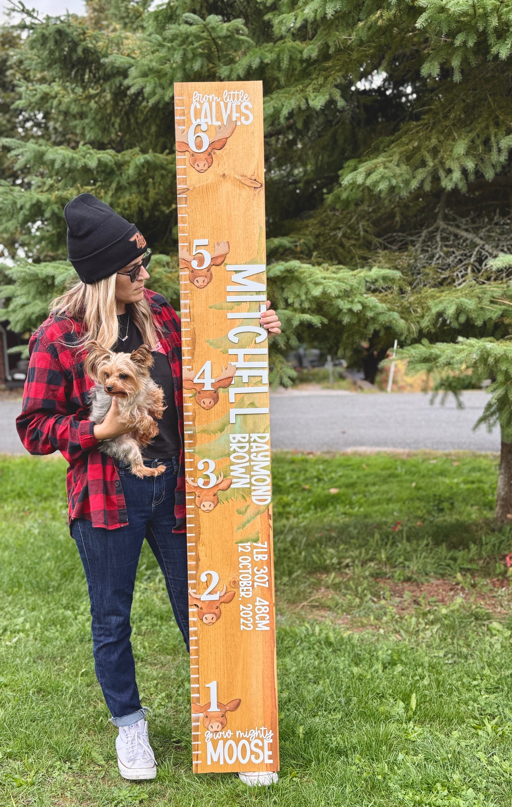 Person holding a large wooden height chart outdoors with trees in the background